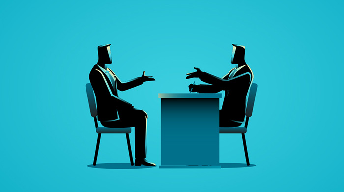 Two people talking at a desk.