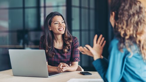 Two women talking next to a laptop/